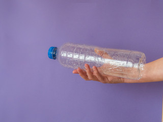 Hand with plastic bottle on purple background with copy space
