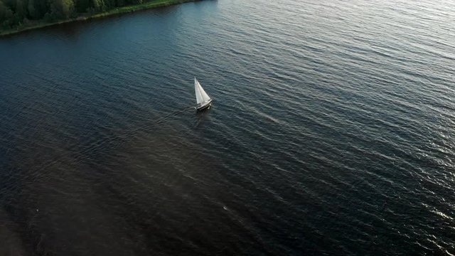 Aerial: Beautiful 4K following a small yacht boat water transport - a bird eye view of Daugava river windy windy weather from above - Drone top view at Sunset