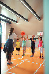 Sports teacher throwing ball to her pupils.