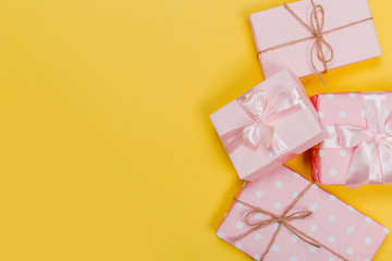 beautiful gift boxes wrapped in paper with red, gold and pink ribbon on a yellow surface. Top view with copy space.