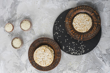 An overhead view of rice grain bowls with stack of puffed rice cake on wooden plate