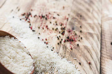 Grain white rice spilling out of round wood bowl with; fresh black peppers over wooden textured surface