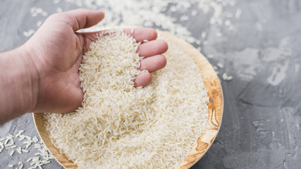 High angle view of a human hand holding raw rice in wooden plate over cement backdrop
