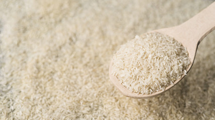 Wooden spoon filled with raw rice over blurry rice backdrop
