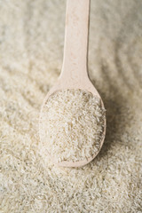 White uncooked rice in wooden spoon over background