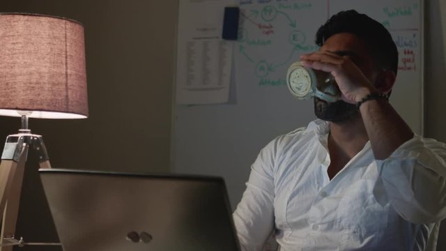 Tired Man Works Back Late in Dark Office at Night, Drinks Coffee - Close Up