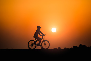 Fototapeta na wymiar Silhouette woman cycling on sunset background