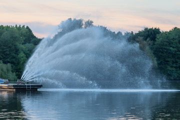 Fountain, beating powerful jets in the middle of the reservoir on the background of a beautiful sunset.
