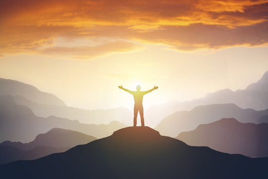 Climber arms up outstretched on mountain top looking at inspirational landscape.
