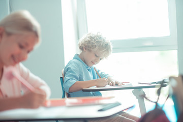 Blond-haired boy sitting near the window in class.