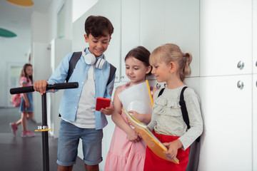 Fototapeta premium Boy holding smartphone showing his favorite game to girls