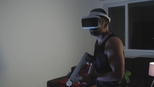 Man Plays Virtual Reality Video Game with Gun and Goggles in Living Room, Night