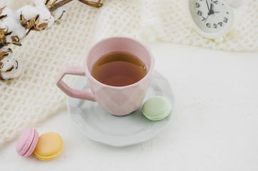 Colorful macaroons with herbal green tea in pink ceramics cup and saucer on desk