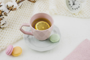 Pink ceramic cup with lemon tea and macaroons on white backdrop
