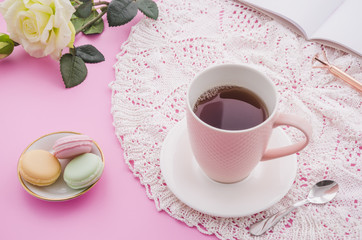 Herbal tea cup with macaroons; spoon; rose; pen and book on pink background