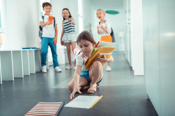 Girl picking up books from floor after boy pushed her