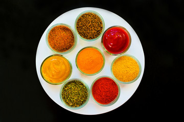 Set of spices and herbs on a white plate. Indian cuisine Pepper, salt, paprika, curry, basil, mustard, nutmeg, turmeric. View from above. Close-up.