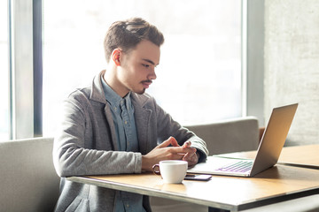 Fototapeta premium Portrait of young successful serious businessman working on computer sitting in office. thoughtful entrepreneur connecting to wireless via computer, intelligent male freelancer work on laptop