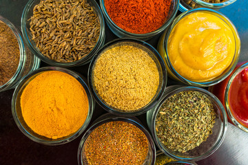  Set of spices and herbs. Indian cuisine Pepper, salt, paprika, curry, basil, mustard, nutmeg, turmeric. On a black wooden board. View from above. Close-up.