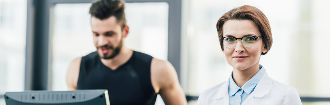 Sportsman Running On Treadmill Near Doctor Looking At Camera During Endurance Test In Gym