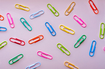 Bright colourful paper clips  laying in disorger on a pink background