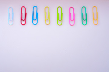 Bright colourful paper clips  laying in a raw on a pink background