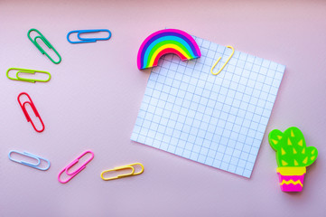 office multi-colored bright neon paper clips, eraser in the form of a rainbow,  cactus and the white empty squared paper sheet on a pink background. Mockup design on a school, educational theme