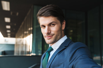Obraz premium Photo of young businessman looking at camera and taking selfie while standing outside job center