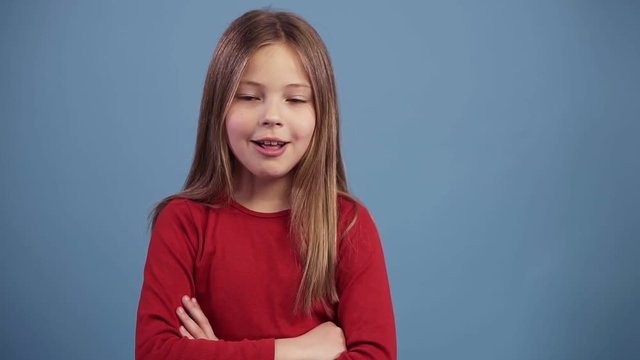 Wow expession. Little caucasian girl in red sweater showing thumbs up and positively smiling, isolated on blue background. Slow motion