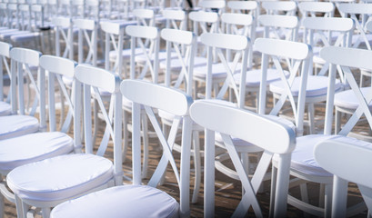 Rows of white chairs in rows on the beach sand. Conference or outdoor wedding. Watching a movie or a street theater.