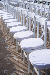 Rows of white chairs in rows on the beach sand. Conference or outdoor wedding. Watching a movie or a street theater.