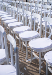 Rows of white chairs in rows on the beach sand. Conference or outdoor wedding. Watching a movie or a street theater.