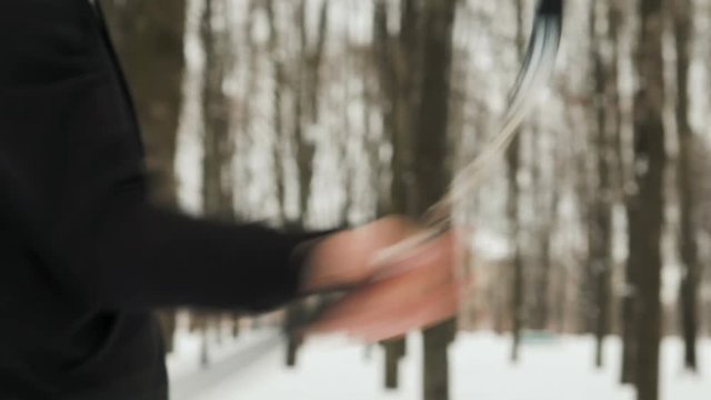 Steadicam shot closeup of the hands of active young men, a fighter of martial arts, dressed in black, performing the technique of blows with nunchaku in the winter, snow covered city Park among the