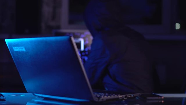 Hacker typing program code while committing a cybercrime hacking a system firewall in the dark under neon light