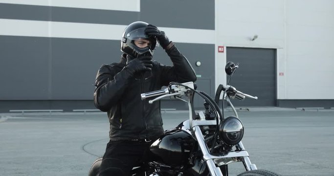 Young man is going to ride a motorbike. Man biker wears a protective helmet sitting on a motorcycle and going to go. He has a cool stylish black motorcycle.