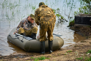 two men fishermen in a rubber boat moored to the shore of the lake with a catch