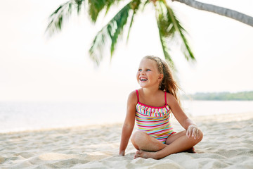 Adorable little girl relax on sandy beach under palm tree with copy space