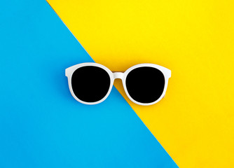 Sunny stylish white sunglasses on a bright blue-cyan and yellow-orange background, top view,...