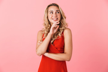 Young pretty blonde cute woman in dress posing isolated over pink wall background.
