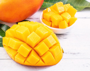 Beautiful chopped mango with green leaves on bright white color timber background. Above Top view,...