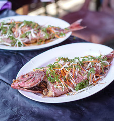 Fried sea fish on a white plate. Seafood in an outdoor cafe in Asia. Stock photo