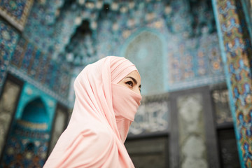 Enigmatic Muslim lady with covered face going to beautiful mosque with ornamental design and looking away