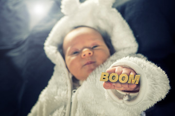 Newborn baby holding up a golden knuckle duster that reads the word BOOM.