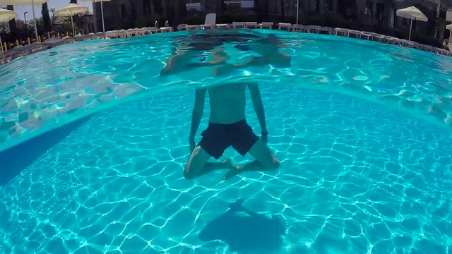 guy in shorts swimming underwater in the outdoor pool