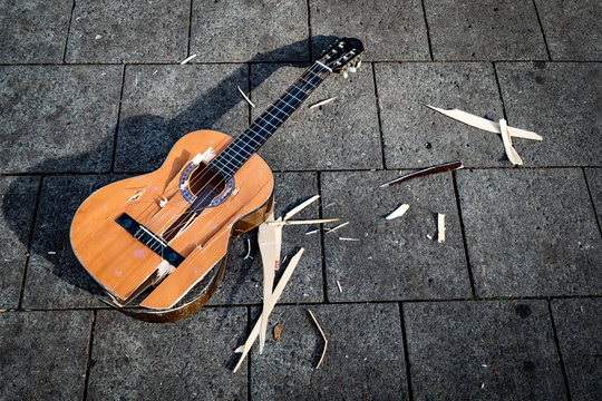 A smashed guitar lies on the pavement.