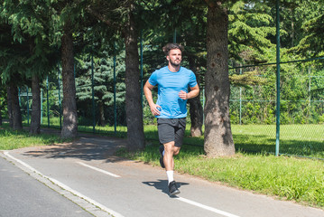 Fototapeta premium Handsome man running in park with trees in background