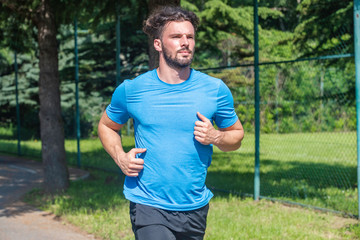 Fototapeta premium Handsome man running in park with trees in background