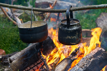 boiler with a teapot in soot hanging on a wooden stick over a blazing bonfire, fresh air