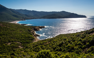A blue ocean bay with a sandy beach lies between green hills - a beautiful seascape.