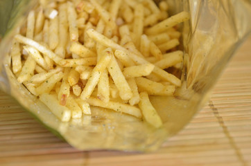 Snack french fries in foil pack. Fried dry potatoes inside packaging on a wooden mat